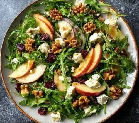 A vibrant Apple Arugula Salad with sliced apples, arugula, and walnuts in a bowl.