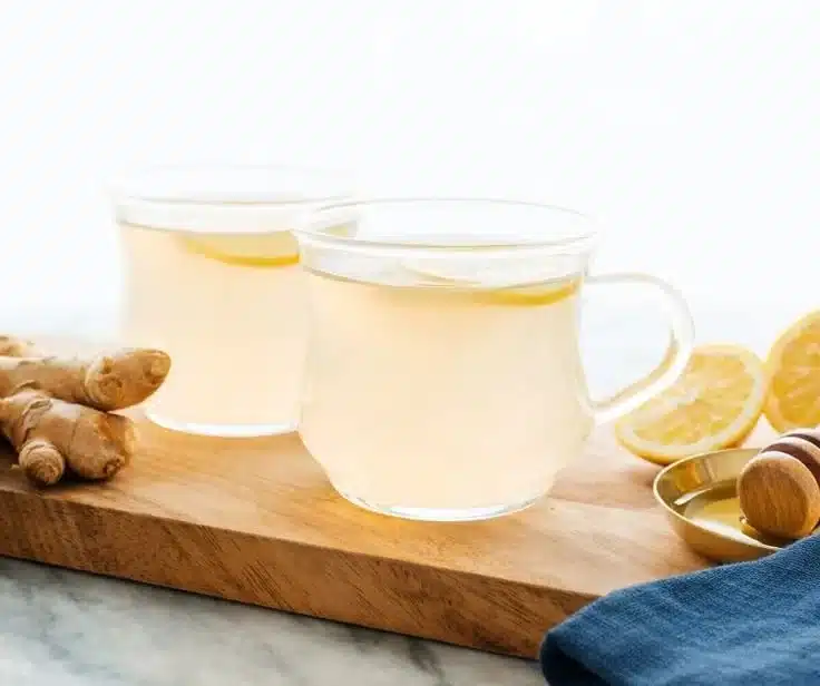 Homemade ginger tea in a cup, tea leaves, and fresh ginger root on the side