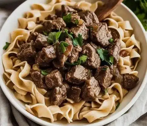 Delicious bowl of hearty beef and noodles, garnished and steaming hot.