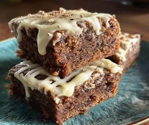 Spiced moist gingerbread brownies with creamy frosting on a decorative plate.